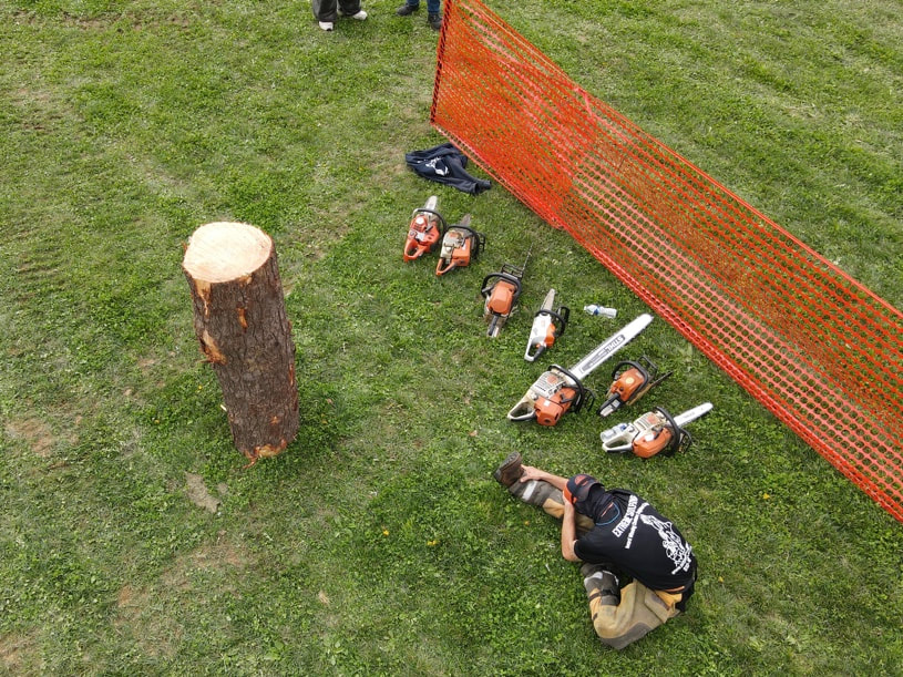 Chainsaw carved sitting with chainsaws and log in a field. He is waiting to begin a competition. 