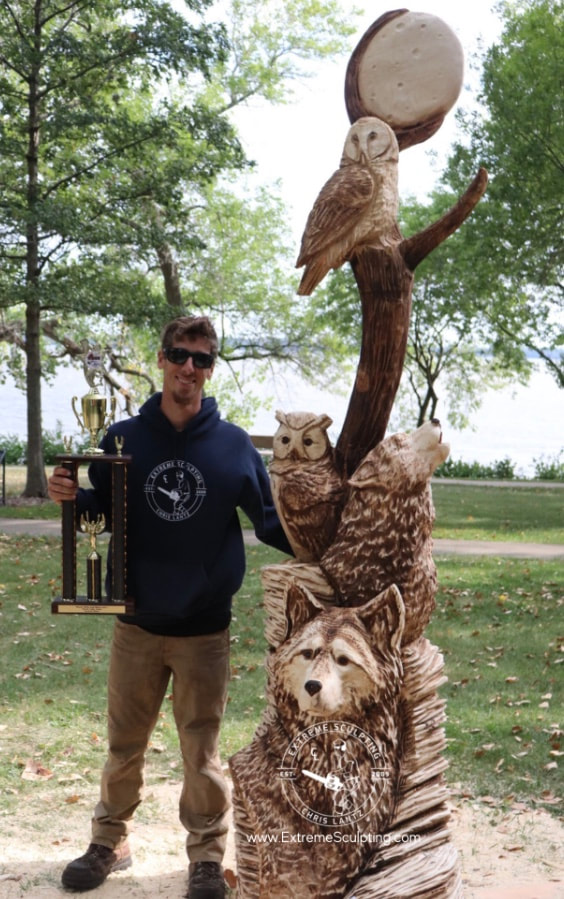 Chainsaw carver standing with owl and wolf carving. 